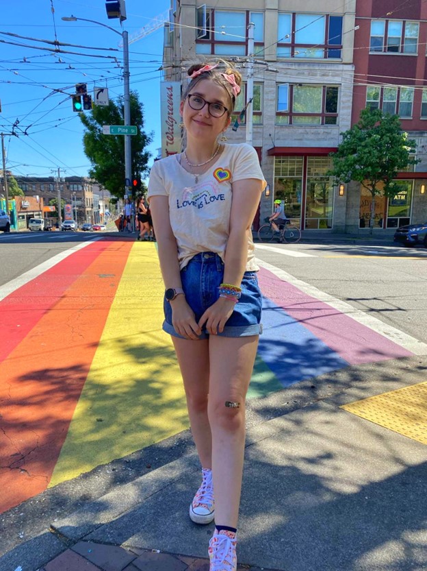 Elizabeth on the corner in front of a rainbow cross walk